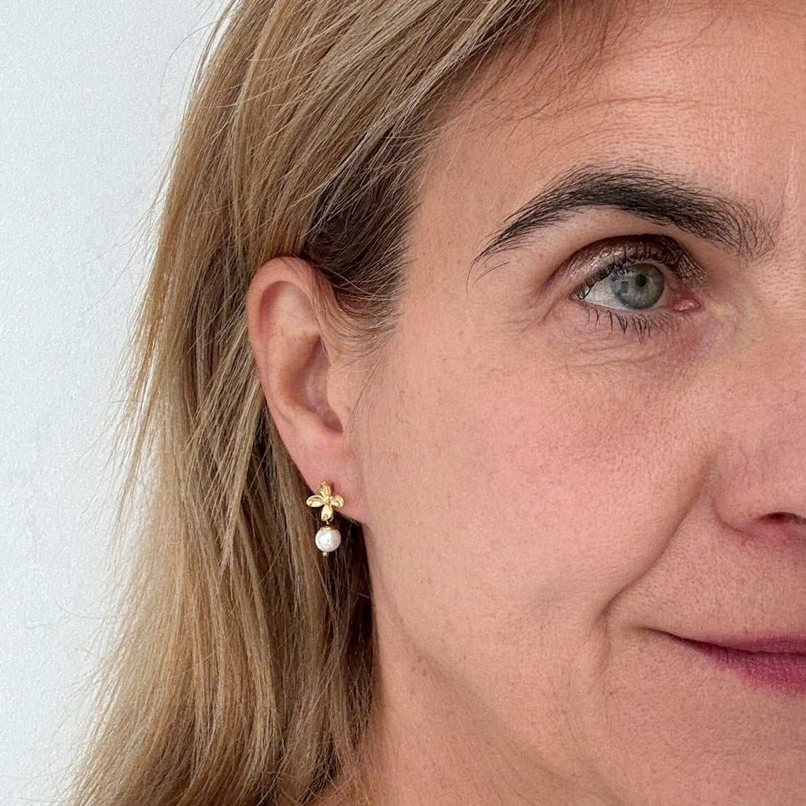 Earrings with gold flower and dangling freshwater pearl worn on model