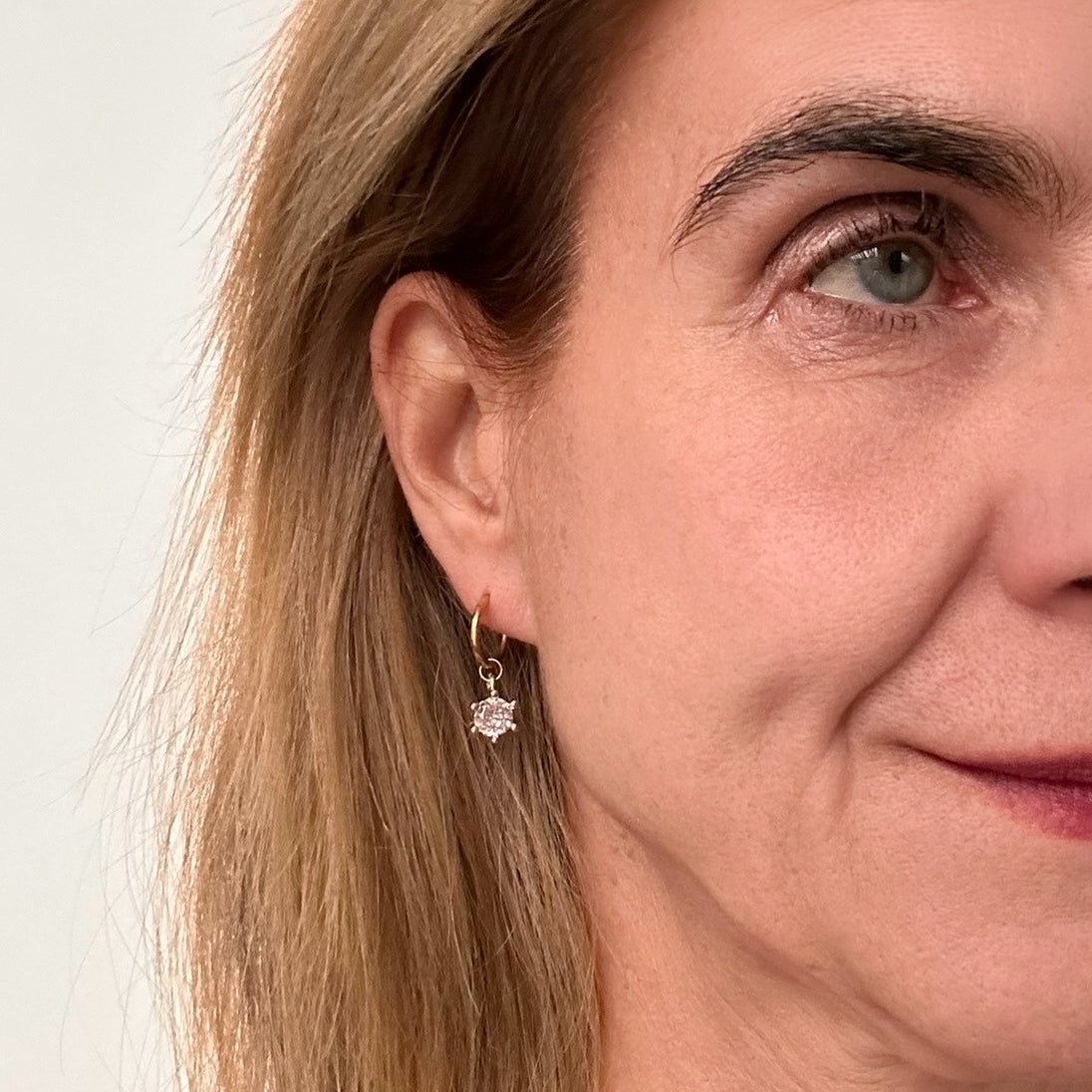 Delicate gold hoop earrings with single sparkly round charms on model