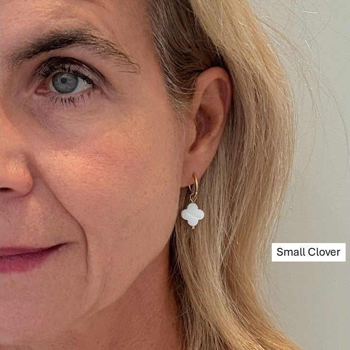 Delicate gold hoop earrings with small clover shaped mother of pearl charms