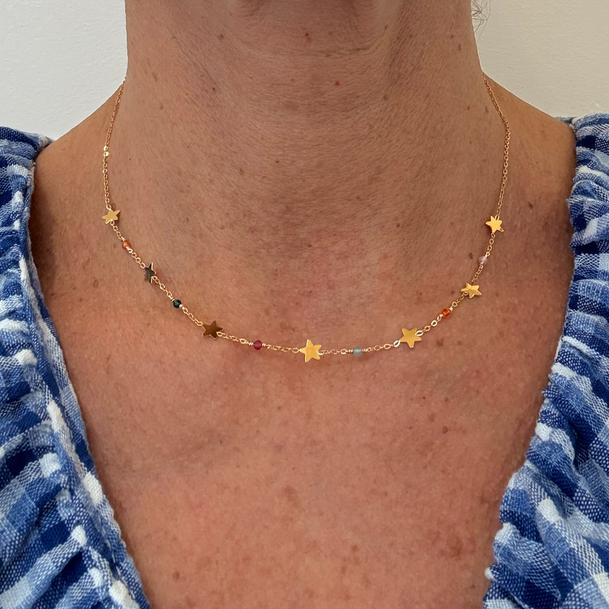 Gold star necklace worn by a person with a blue and white patterned garment.