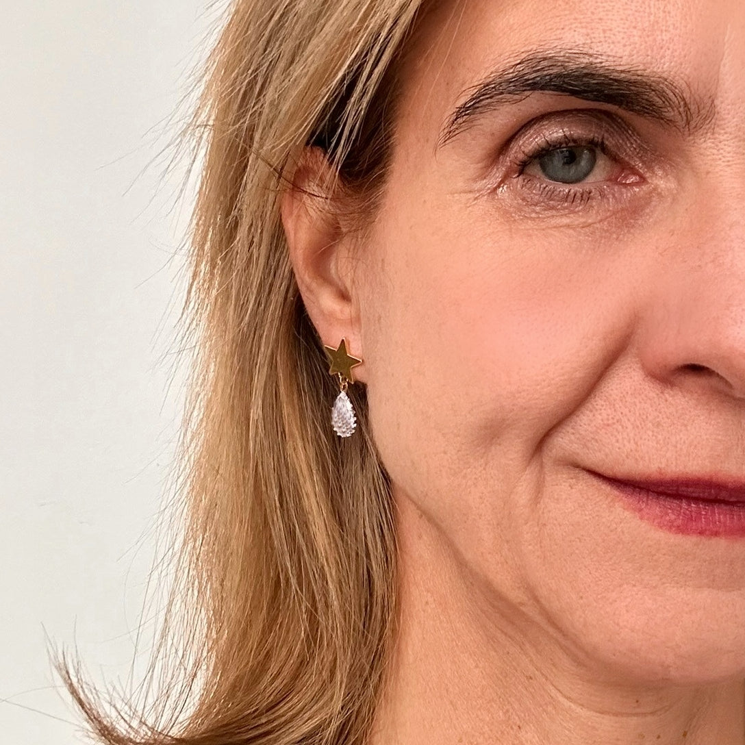 Star shaped gold stud earrings with one oval dangling sparkly crystal on model.