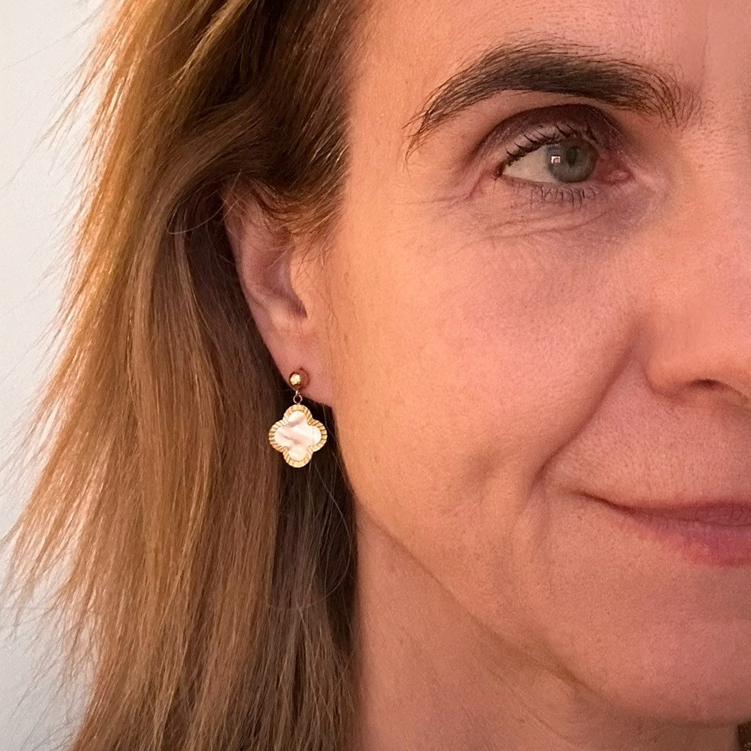 Gold stud earrings with dangling large clover shaped mother of pearl shell charms worn on model