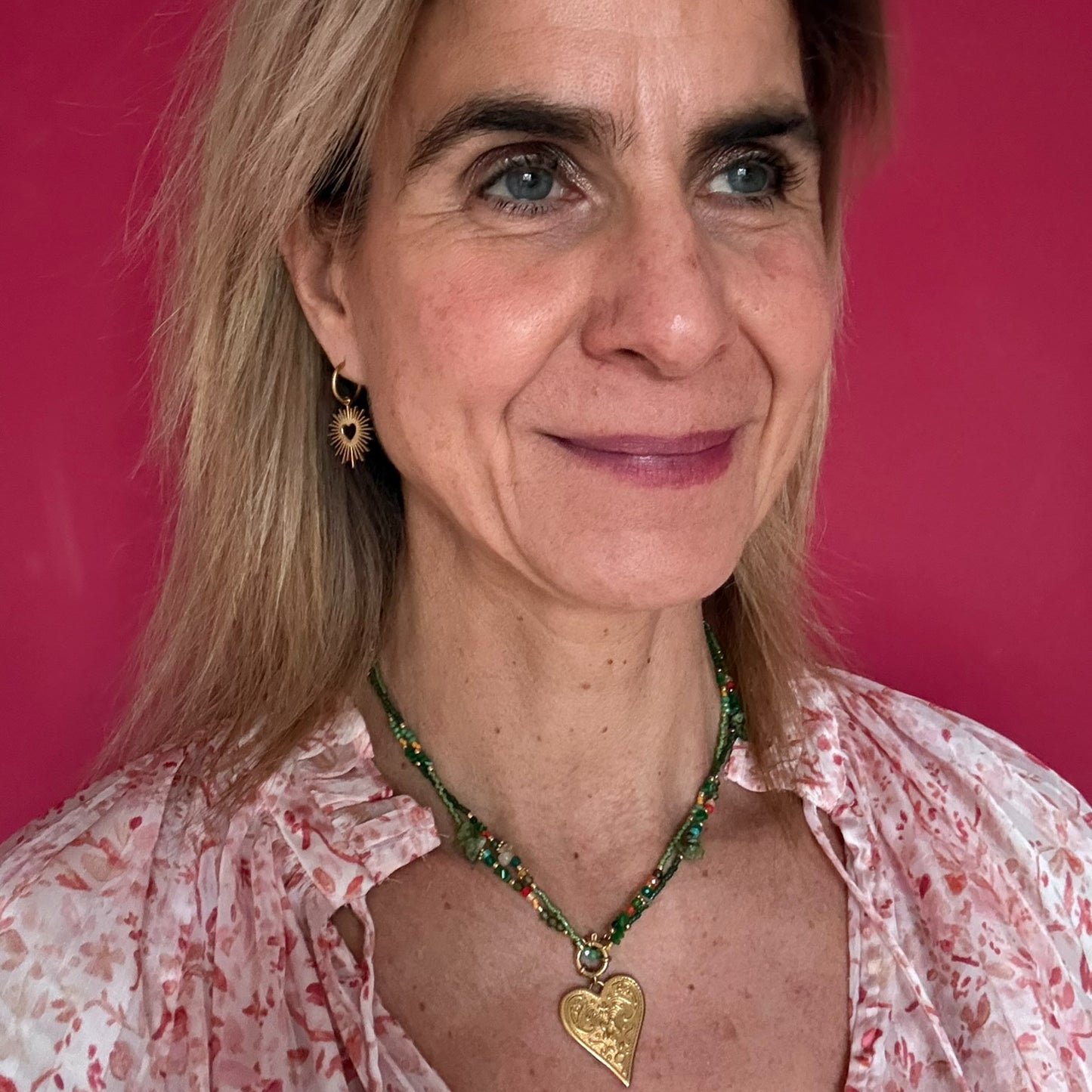 Woman wearing a necklace with a heart pendant against a pink background