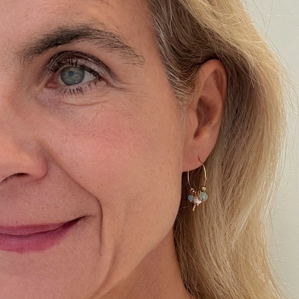 Close-up of a woman wearing gold hoop earrings with small round stones.