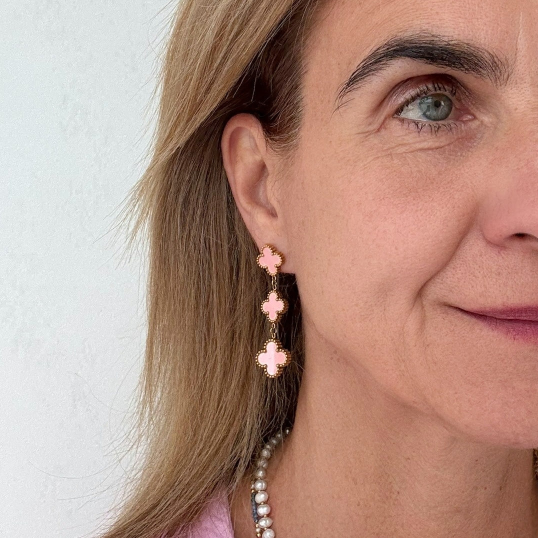 Clover shaped stud earrings with two dangling clover shaped charms all in pink worn on model