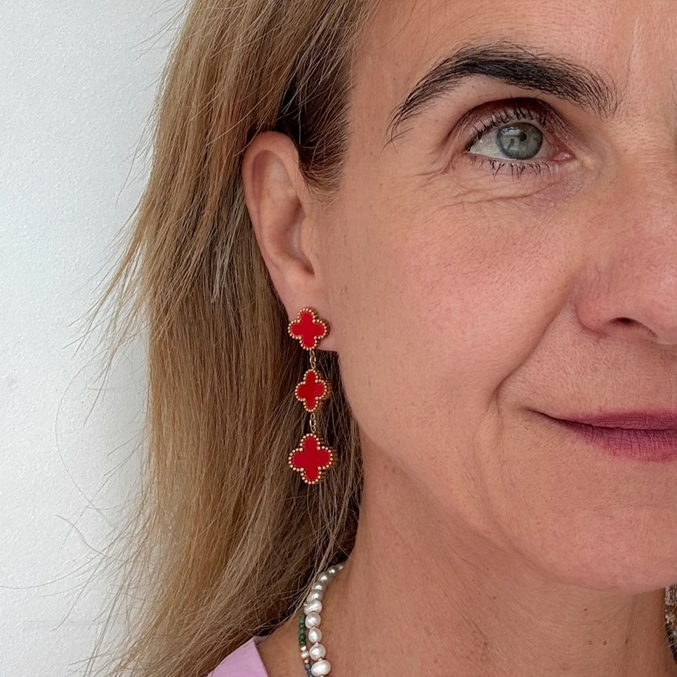 Clover shaped stud earrings with two dangling clover shaped charms all in red worn on model