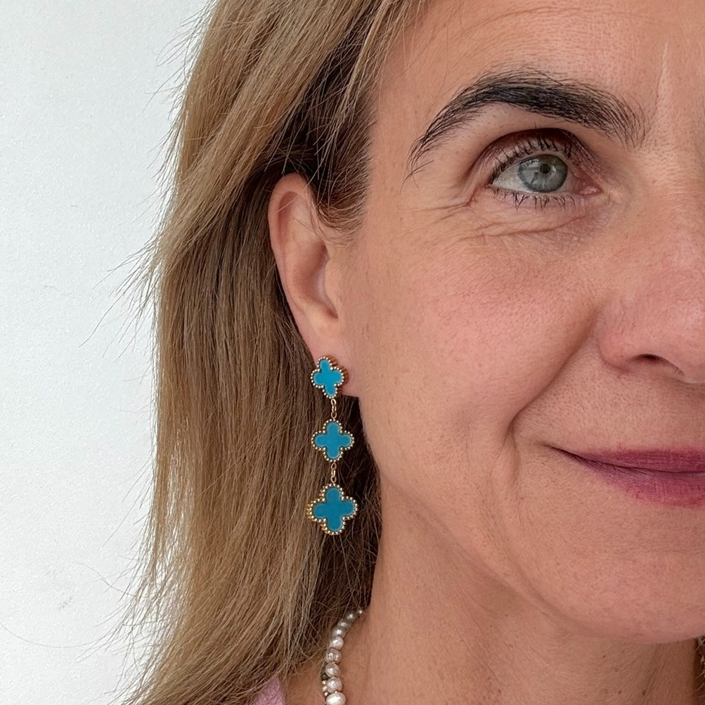 Clover shaped stud earrings with two dangling clover shaped charms all in blue worn on model