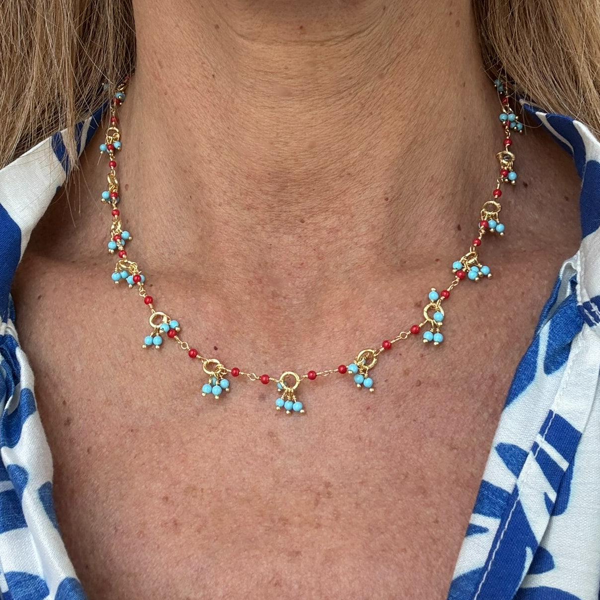 Gold necklace with bright Turquoise and red Coral gemstone beads arranged in clusters worn on model