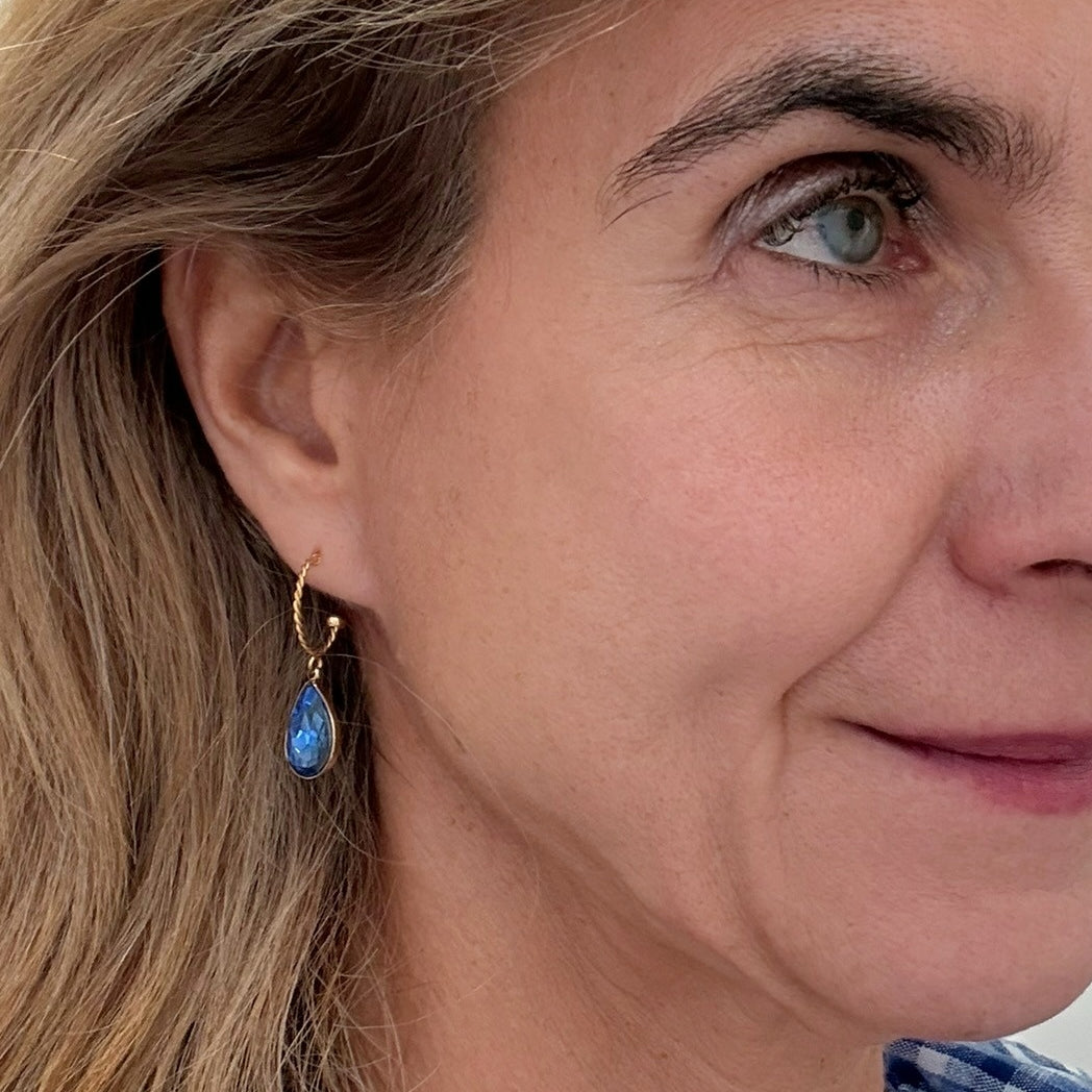 Twisted gold hoop earrings with sparkly blue crystal charm on model