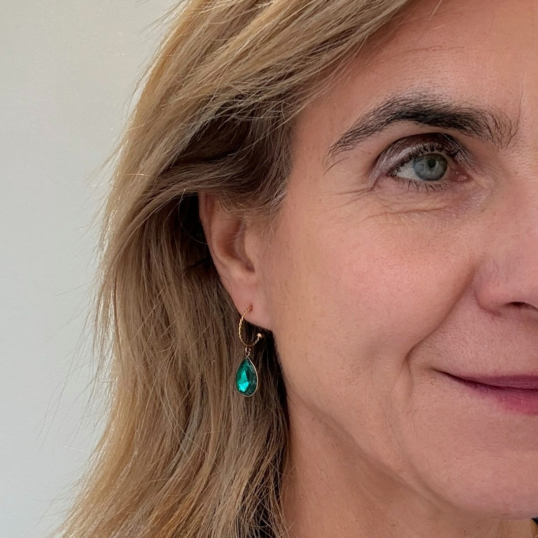Close-up of a woman wearing a gold hoop earring with a green crystal
