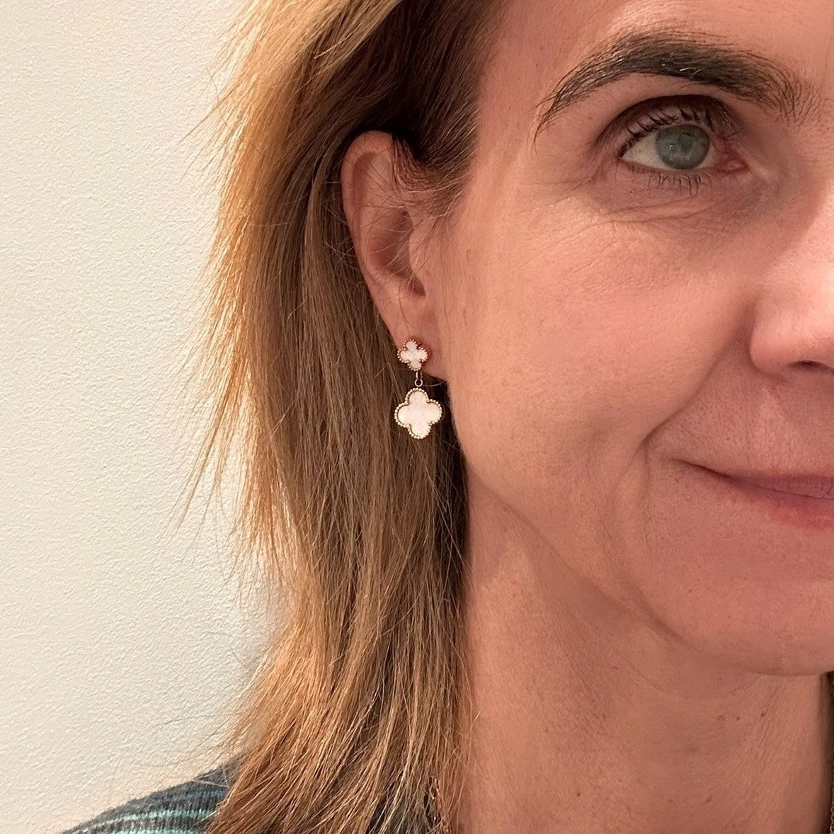 Clover shaped stud earrings with dangling clover shaped mother of pearl charm on model