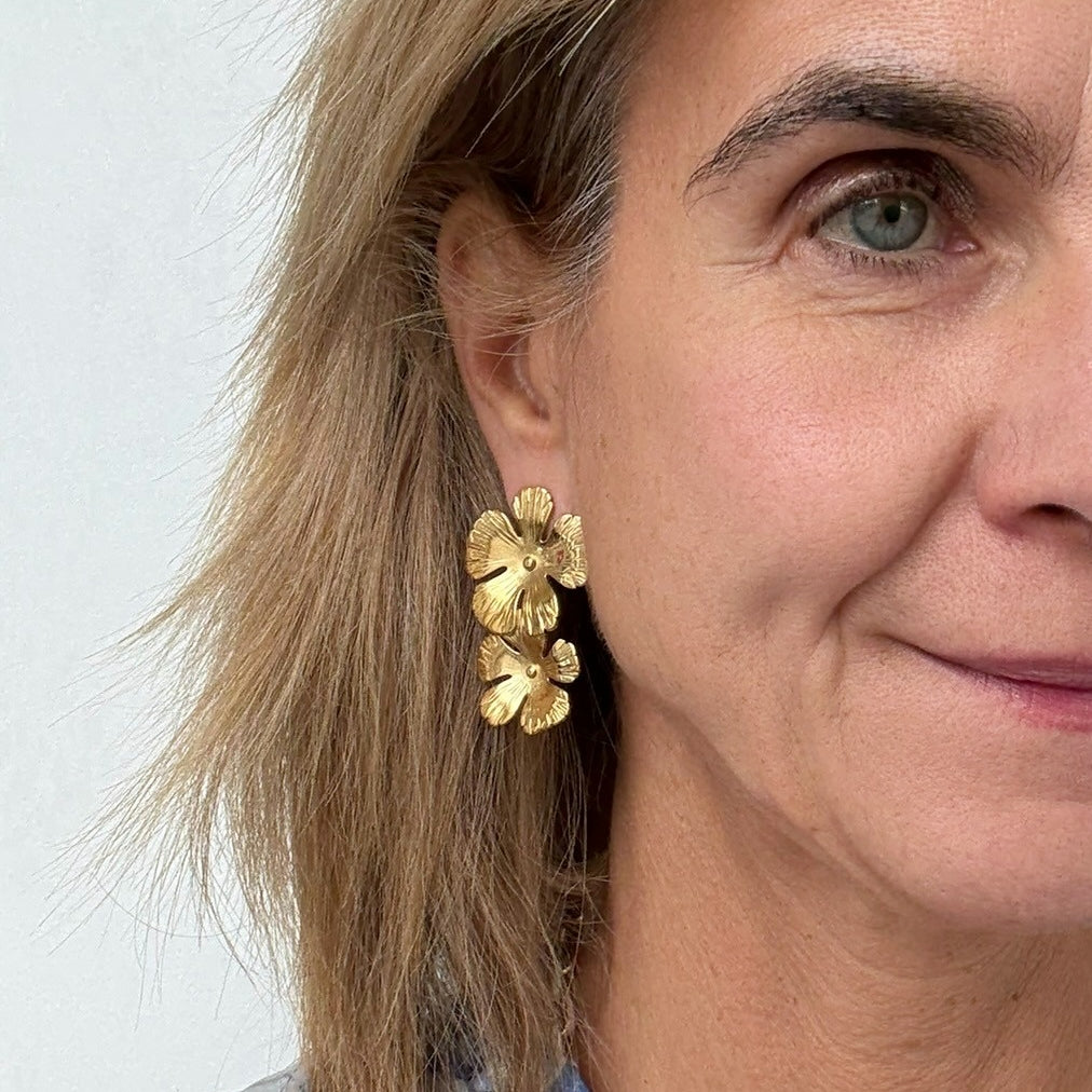 Close-up of a woman wearing gold floral earrings against a light background