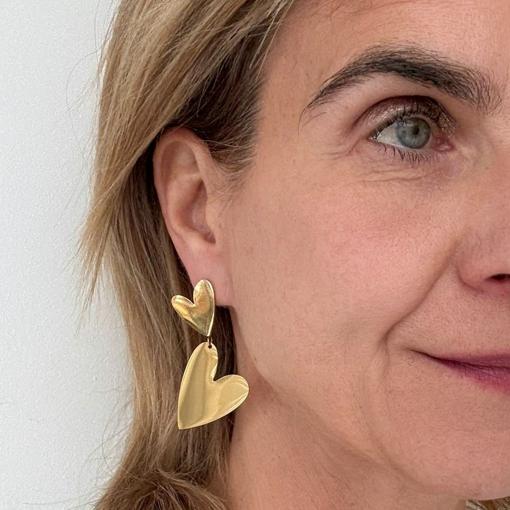 Big bold dangling gold earrings with two hearts worn on model