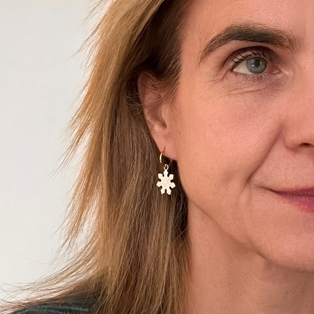 Delicate gold hoop earrings with white snowflake shaped charms worn on model