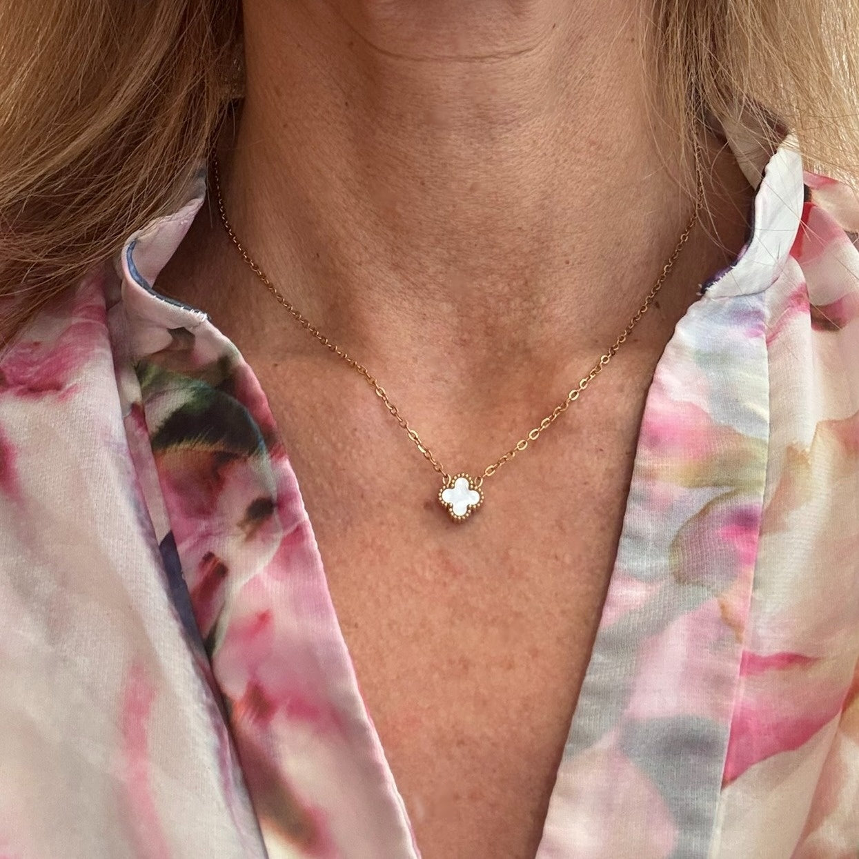 Delicate gold chain necklace with tiny 9mm white clover charm in the middle worn on model