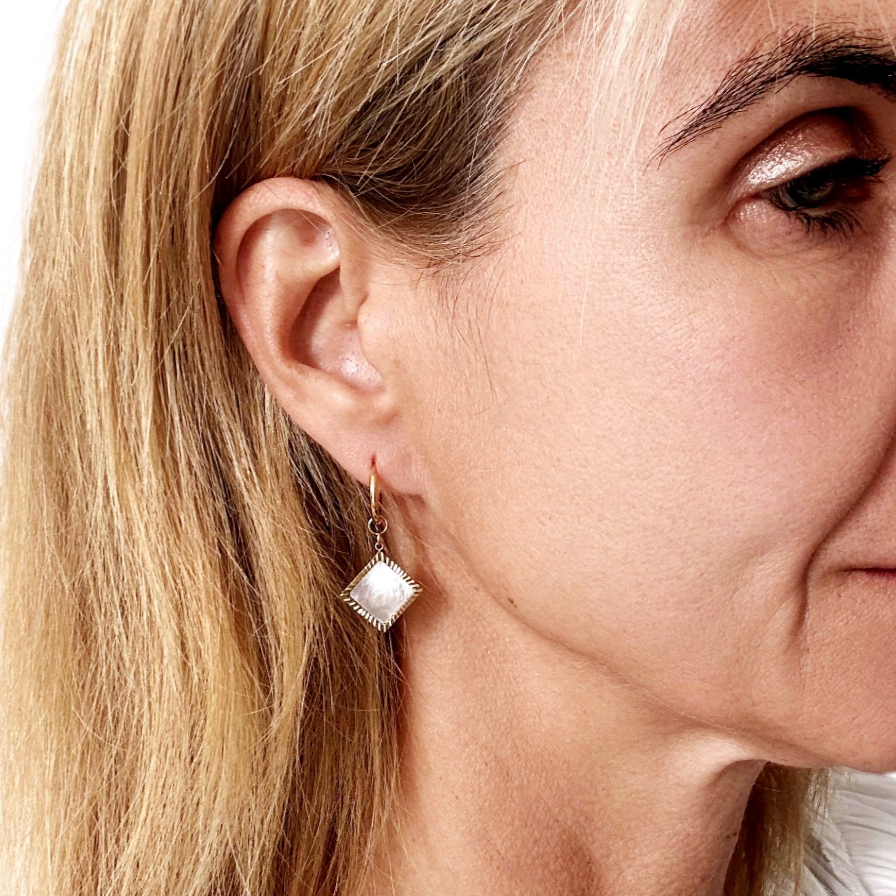 woman wearring gold hoops with diamond shaped mother of pearl charms