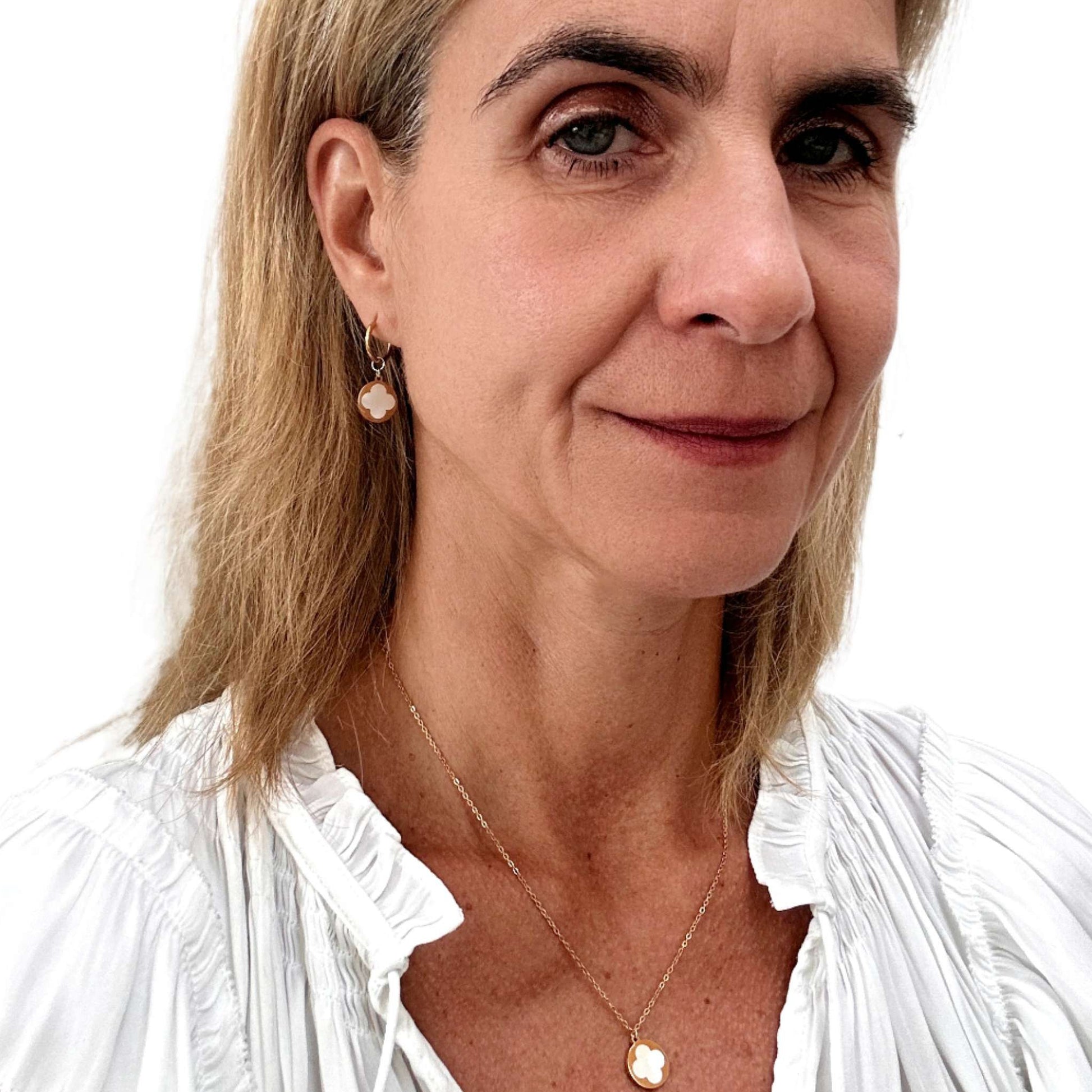 gold hoop earrings with clover shaped mother of pearl shell charms in a gold circle worn on model