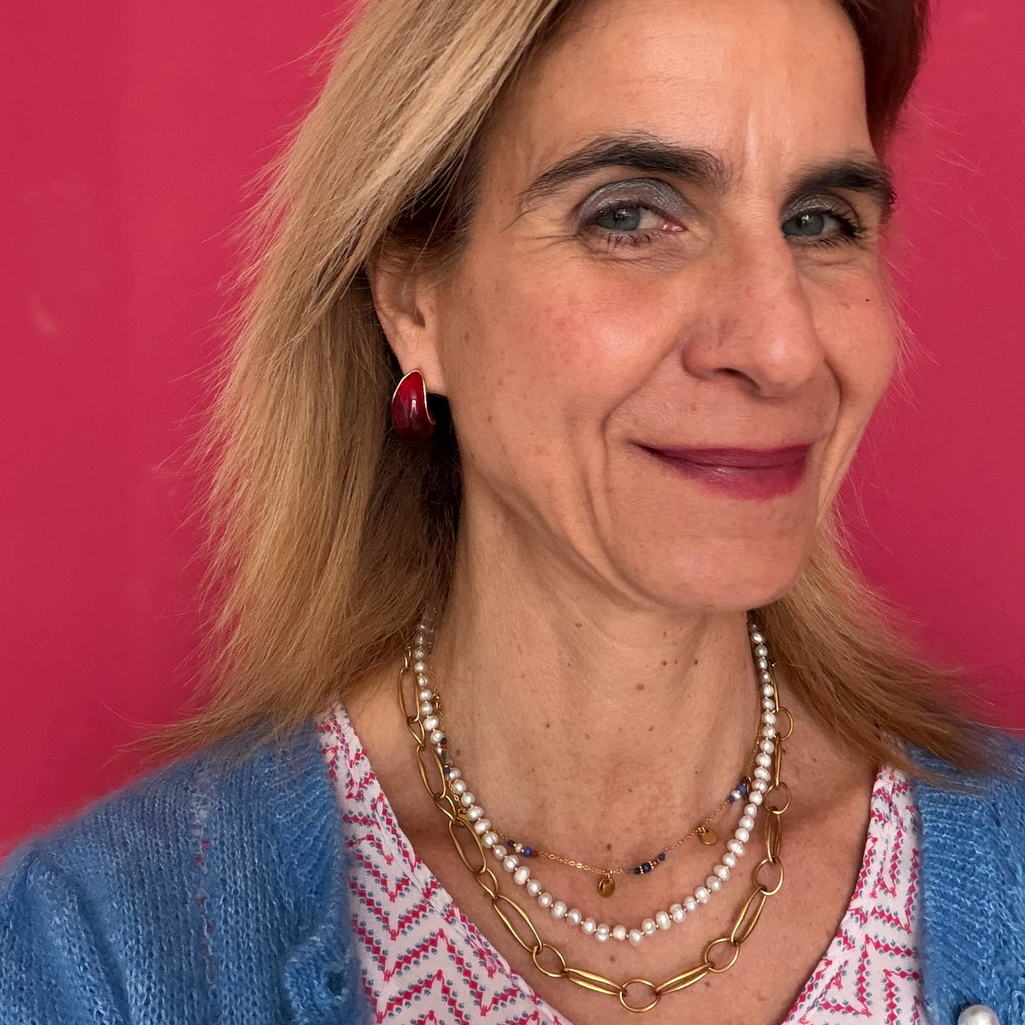 Woman wearing a blue cardigan and pearl necklace against a pink background