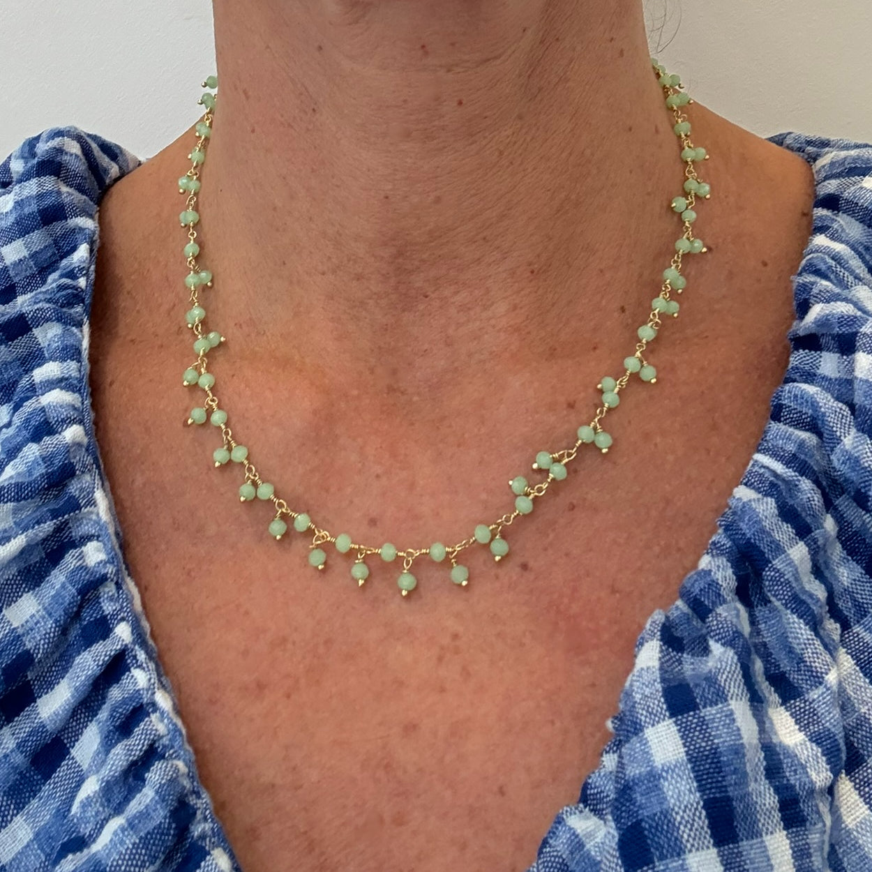 Person wearing a green beaded necklace with a blue and white checkered garment.
