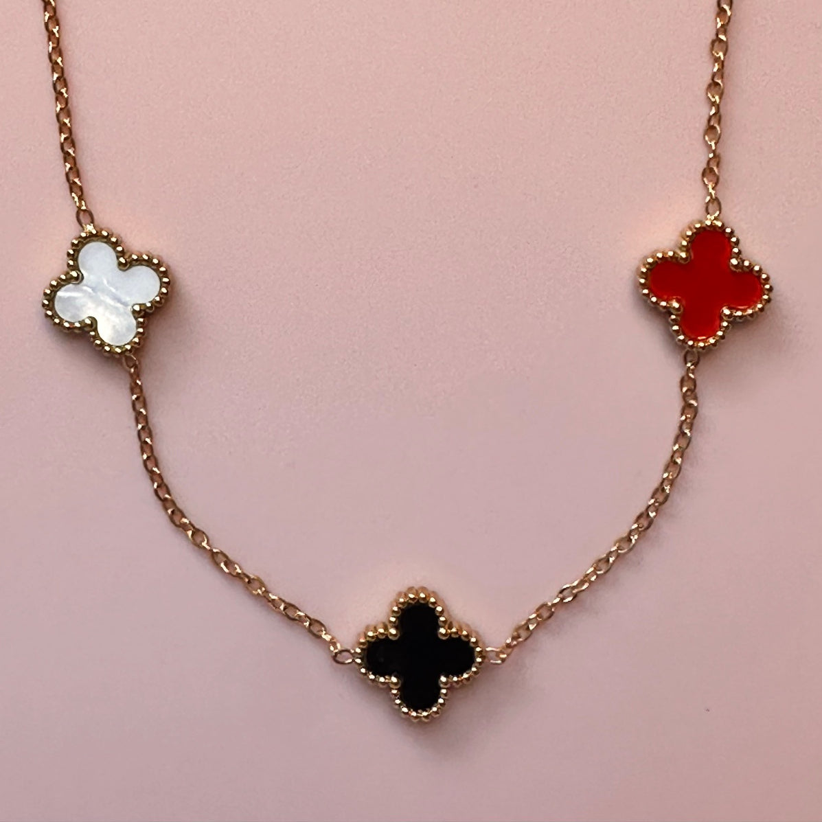 Gold chain necklace with five small clover charms in a rainbow of colours showing 3 of the charms