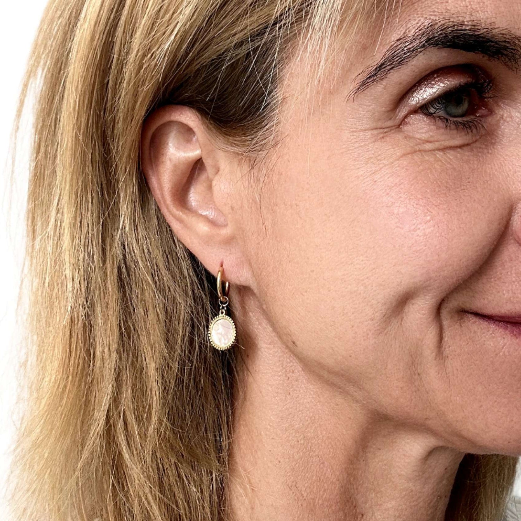 Woman wearring gold hoop earrings with mother of pearl small gold round shaped charms