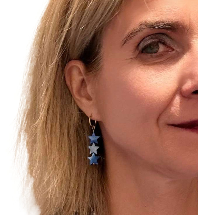 Close-up of a woman wearing blue star earrings with a white background