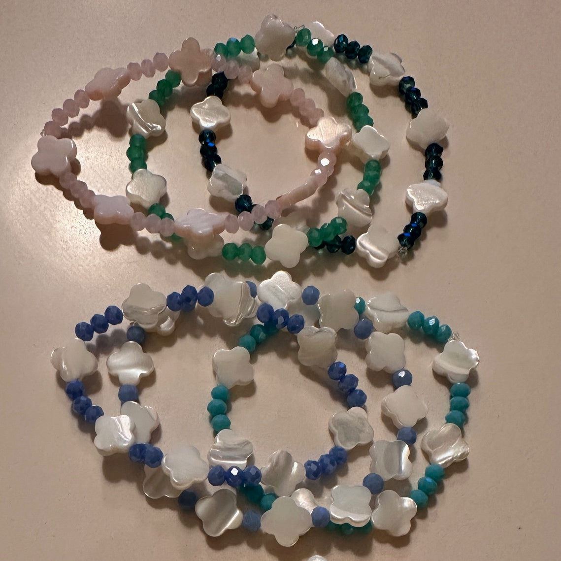 Set of beaded bracelets with white, green, blue, and black beads on a beige background