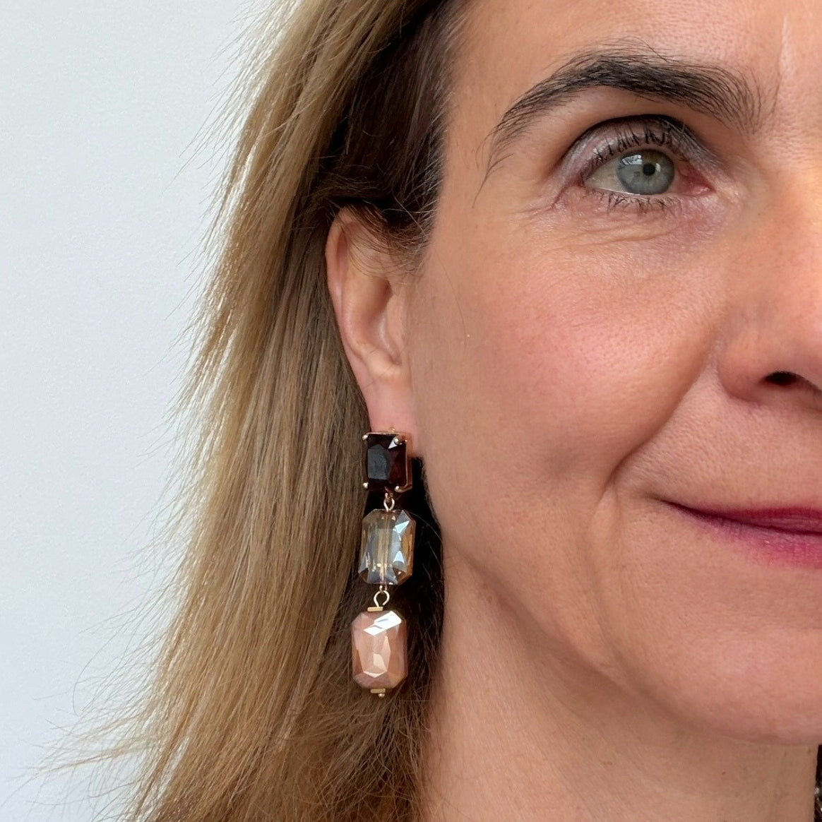 Close-up of a woman wearing big beihe and brown crystal earrings with a white background