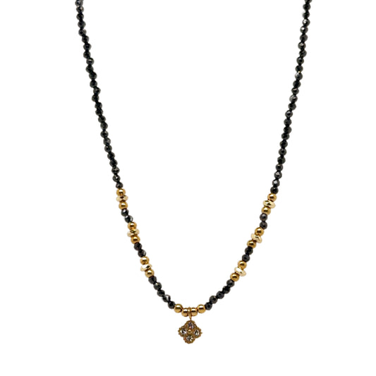 Delicate necklace with tiny black and gold beads, and dangling small sparkly clover charm