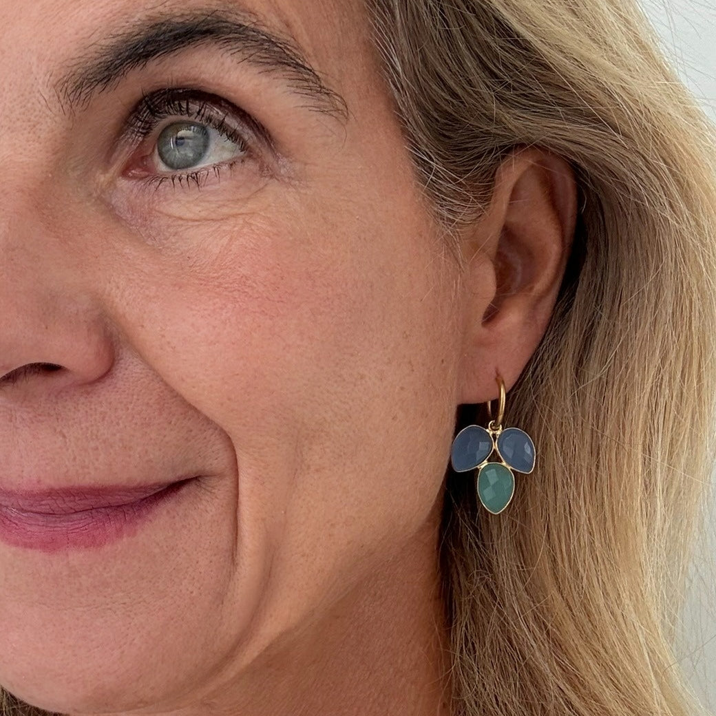 Close-up of a woman wearing a gold earring with blue and green gemstones.