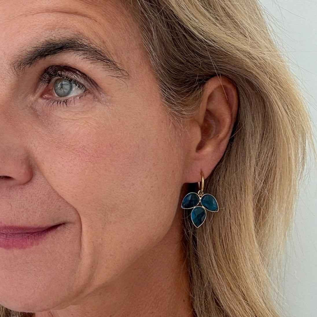 Close-up of a woman wearing blue floral earrings with a neutral background
