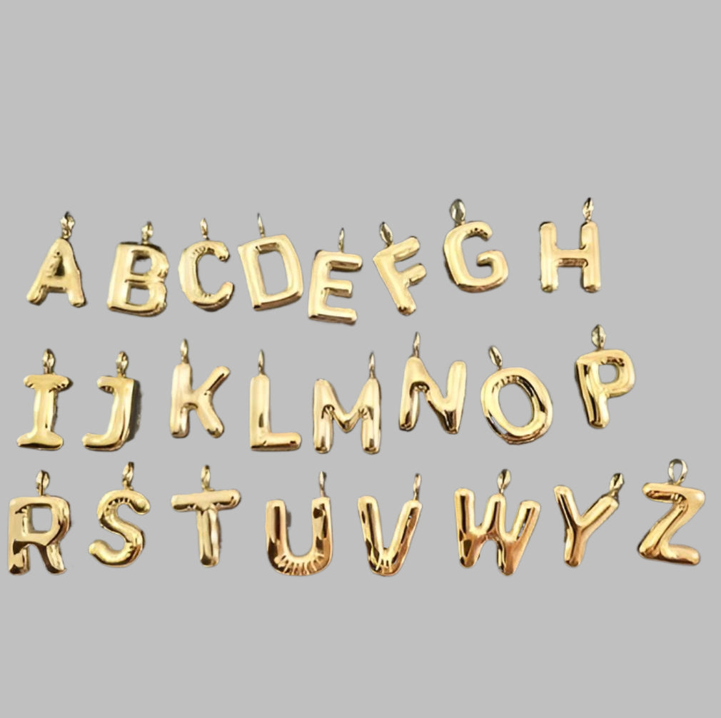 Thirty gold-colored metallic alphabet letter charms, arranged in three rows of ten on a solid gray background.