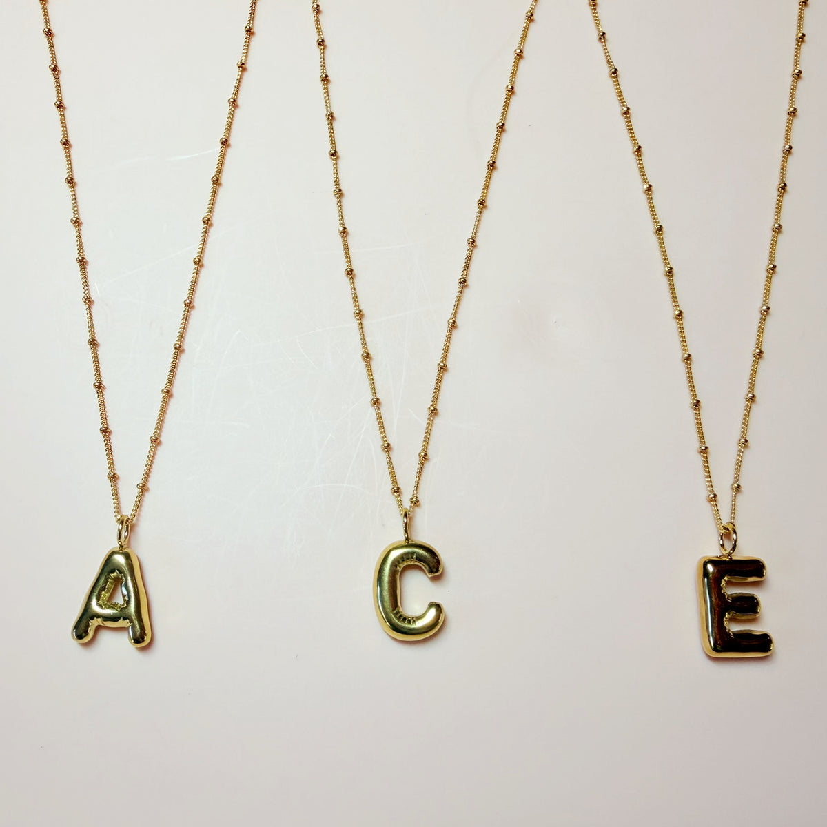 three gold necklaces each with a bubble letter pendant