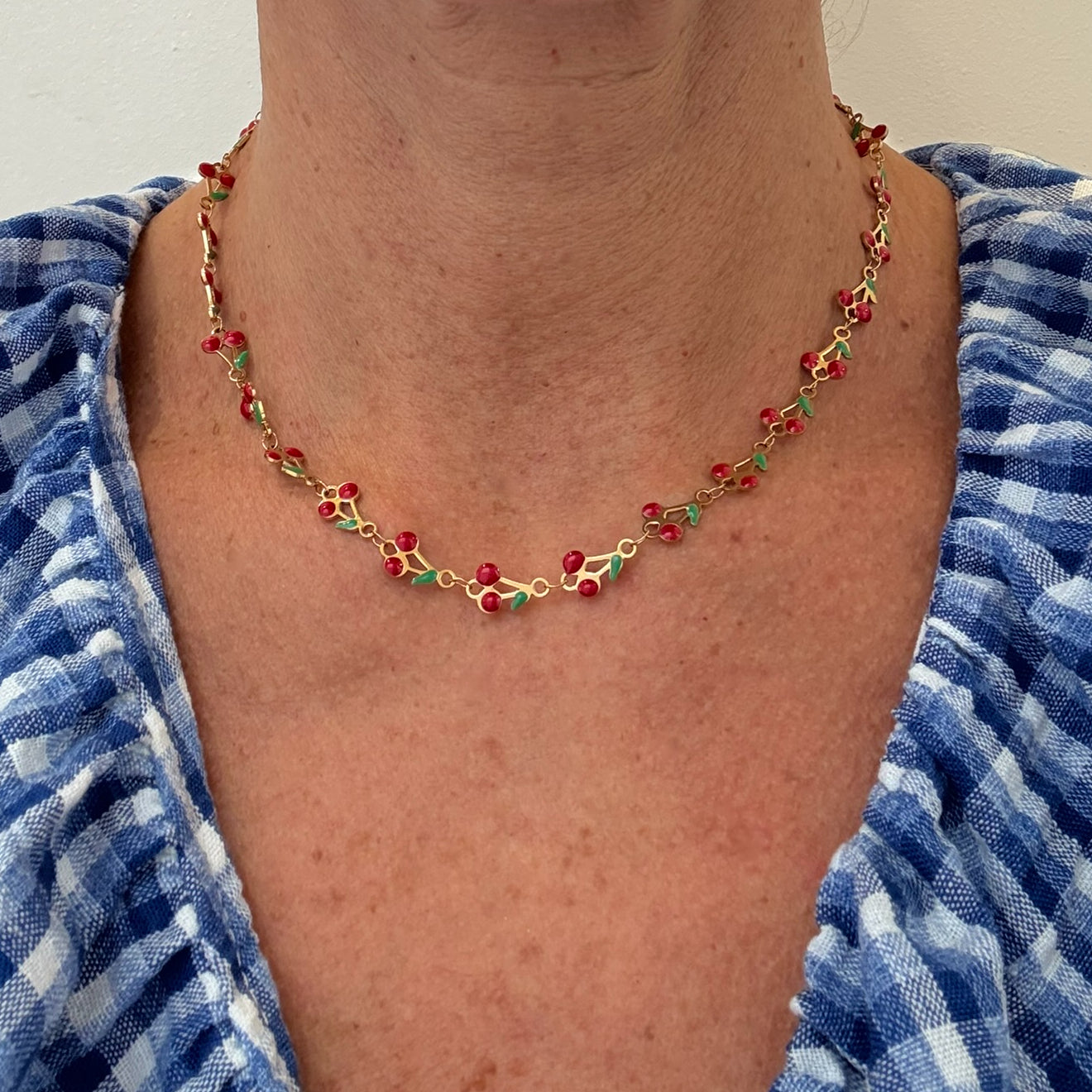 Necklace with red, gold and green cherry charms worn by a person in a blue and white patterned garment.