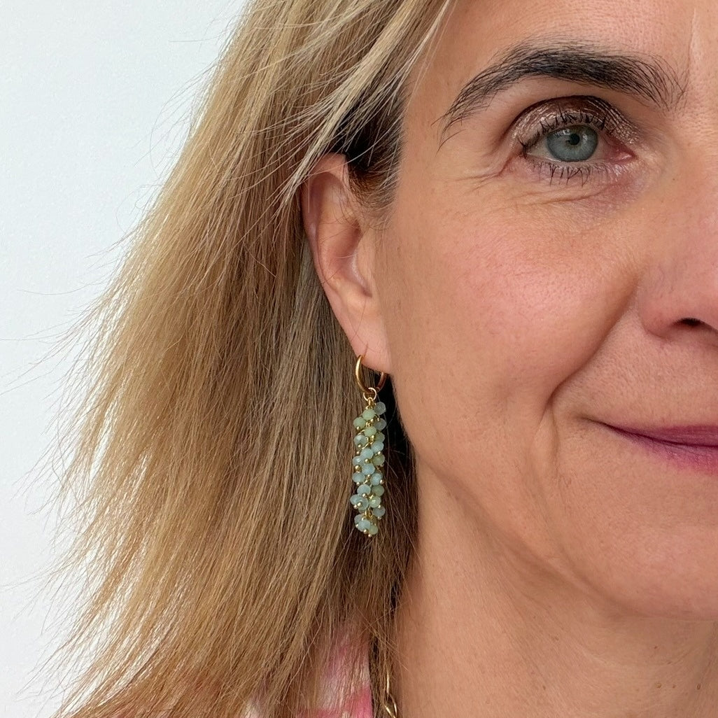 woman wearing gold hoop earrings with  dangling green and blue beads