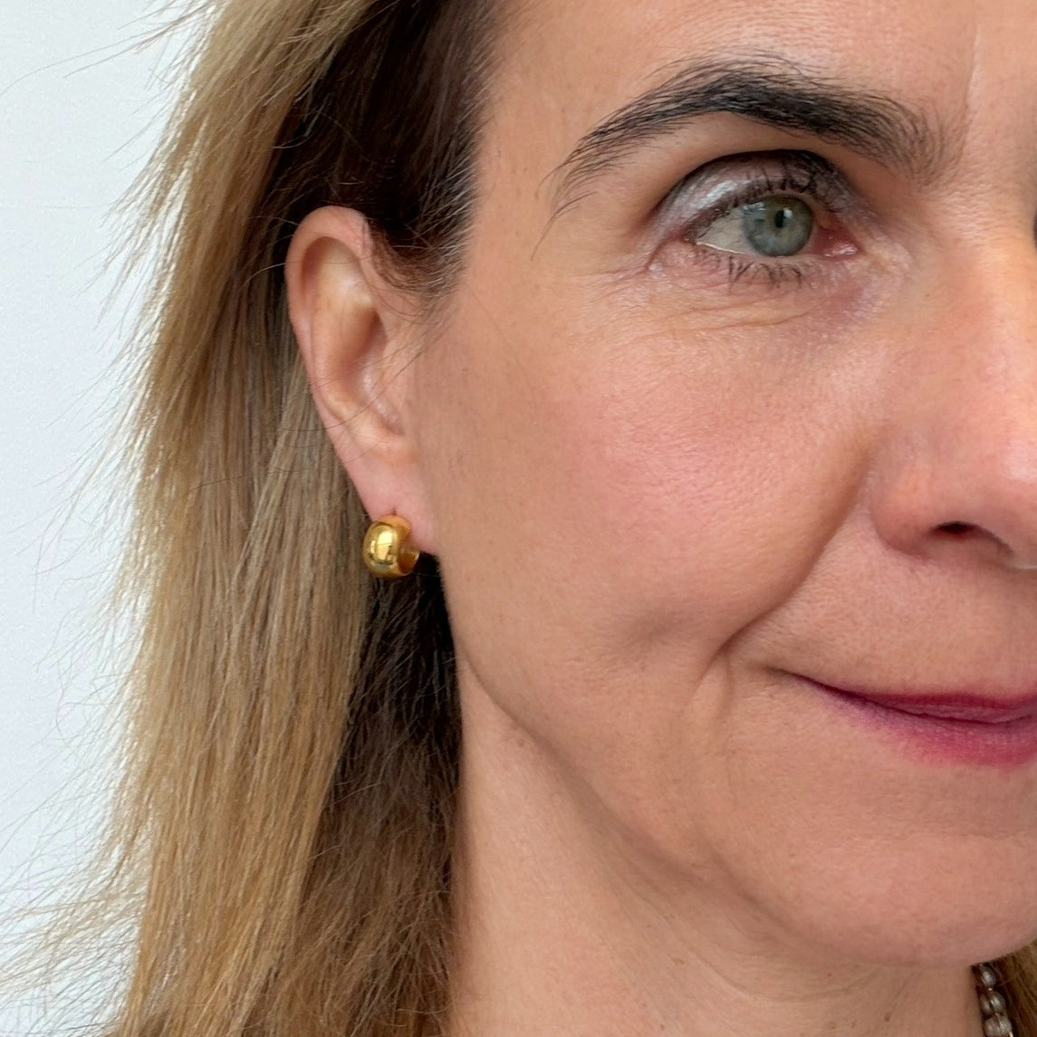 Close-up of a woman wearing small curved gold earrings with a plain background