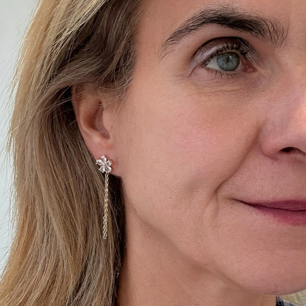 flower-shaped sparkly stud earrings with dangling chain worn on model