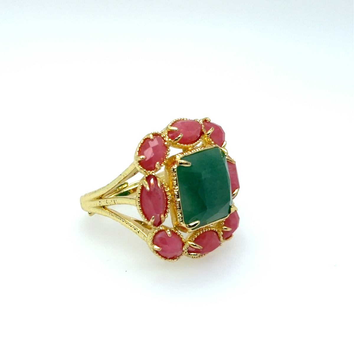 A gold ring featuring a central rectangular green emerald-cut stone surrounded by six oval pinkish-red cabochon stones, set on a plain white background.