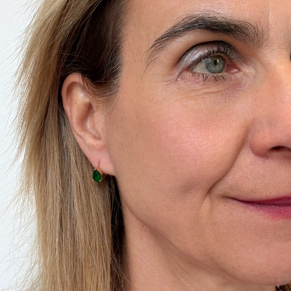 Close-up of a woman wearing green earrings with a neutral background
