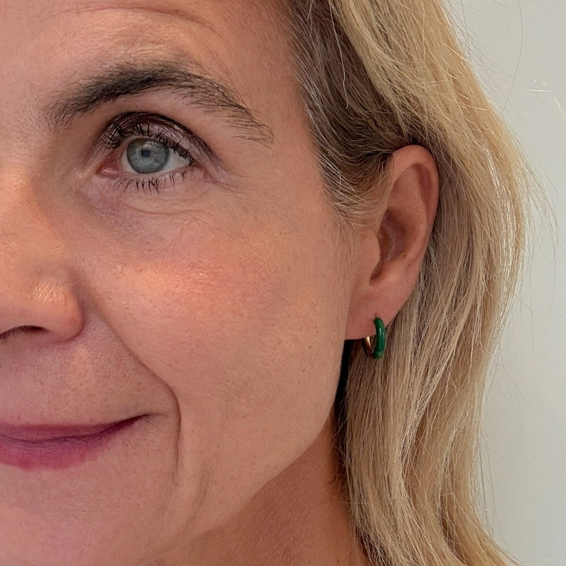 Close-up of a woman's face with blonde hair and green earrings.