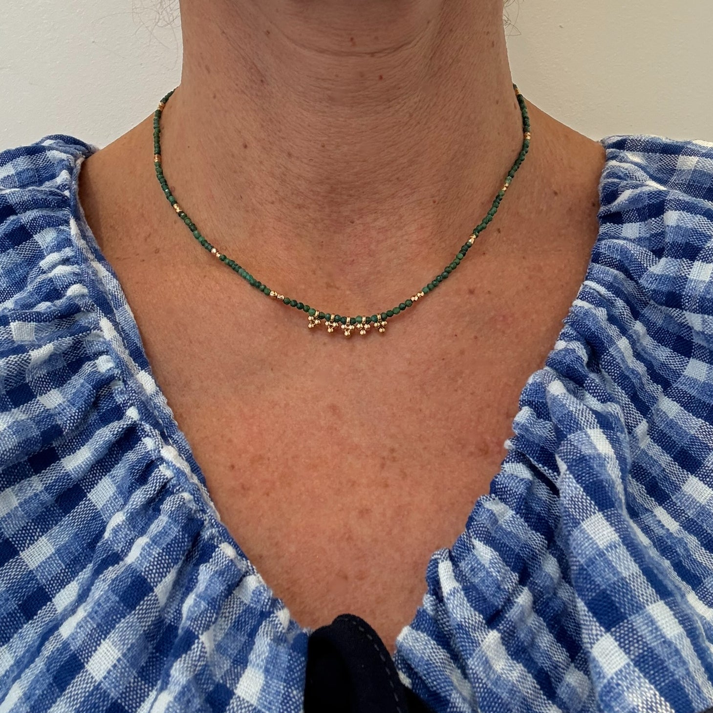 Delicate necklace with dark green and gold beads worn on person