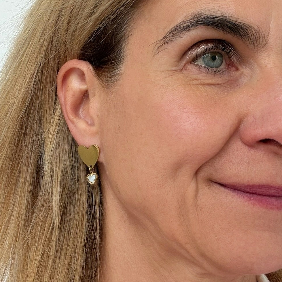 woman wearing gold heart earrings with dangling mother of pearl heart charms