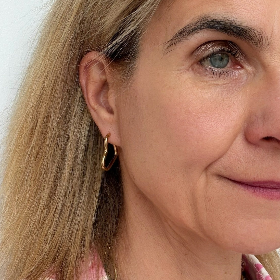 woman wearing gold hoop earrings in the shape of a heart