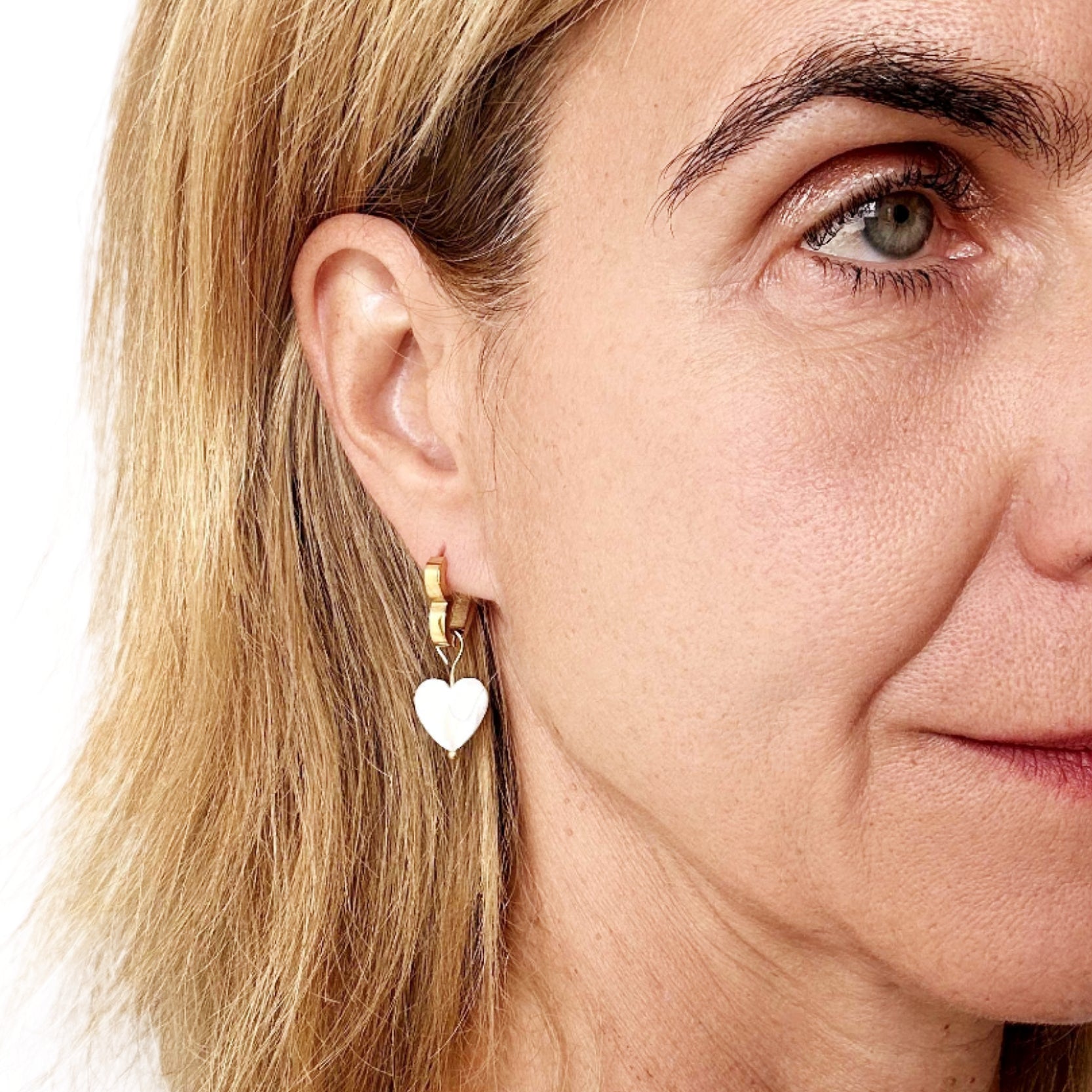 Close-up of a woman wearing gold heart-shaped earrings with a plain background