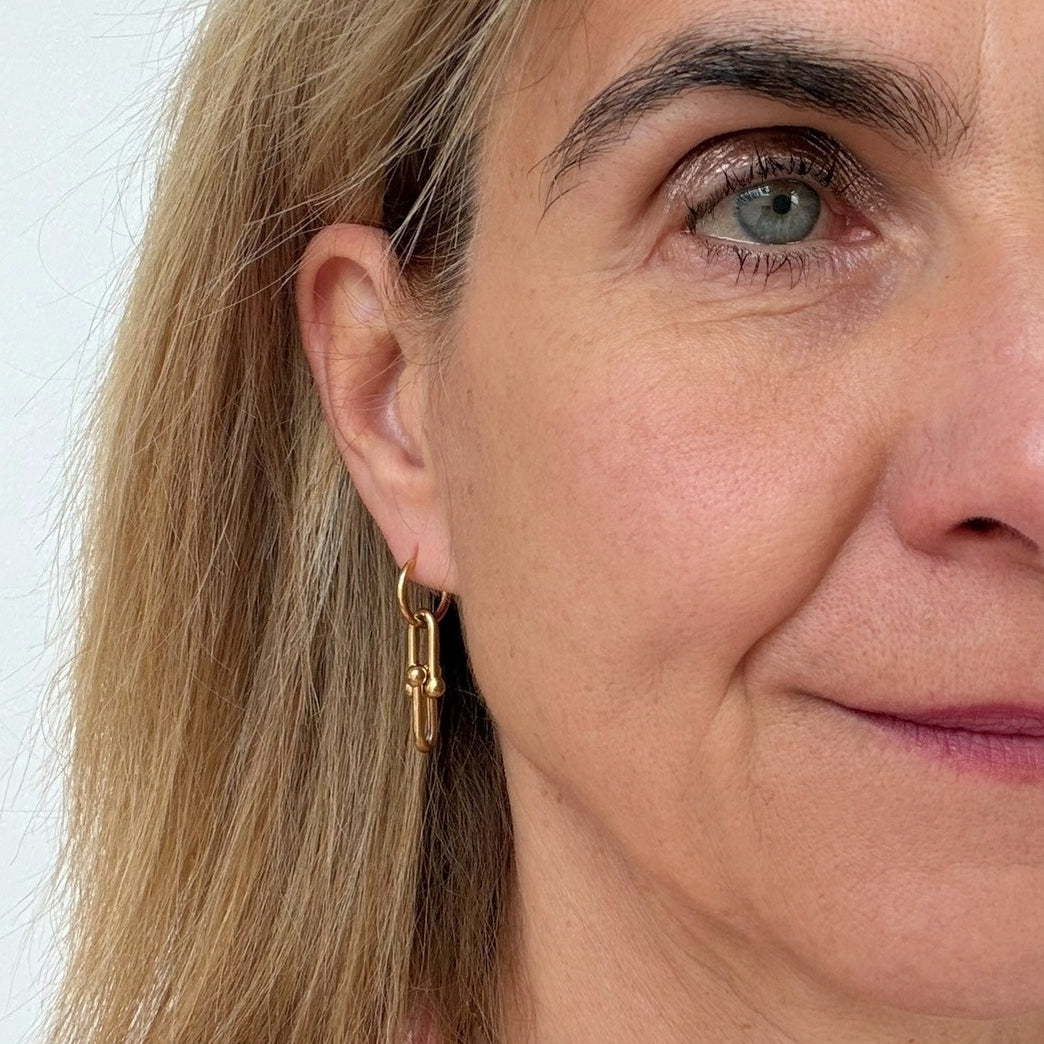 woman wearing dangling gold hoop earrings with two ball chain links