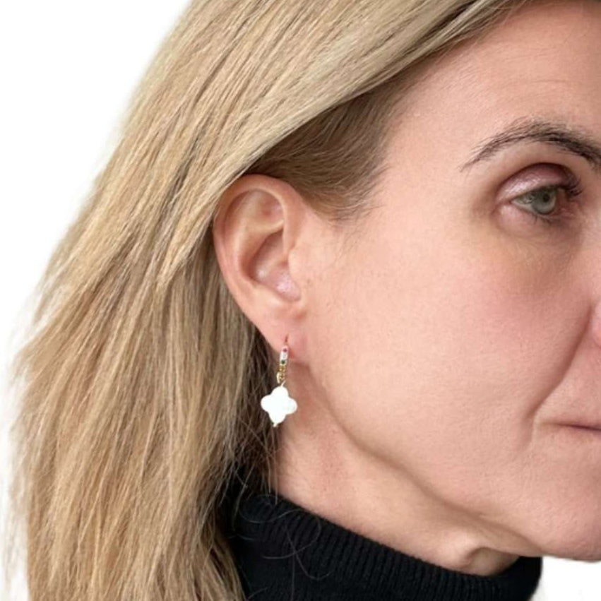 Close-up of a woman wearing gold earrings with a white nother of pearl clover shaped charm