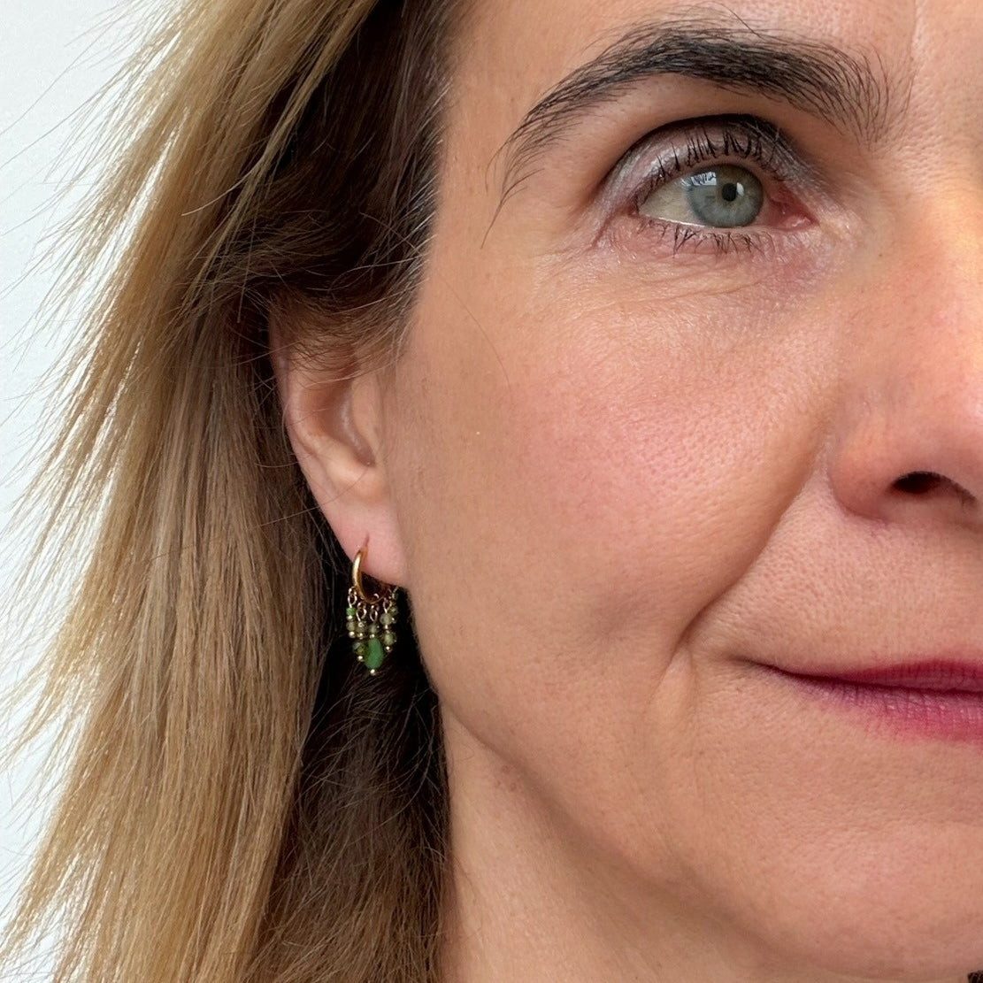 Woman wearing gold hoop earrings with small green crystal charms