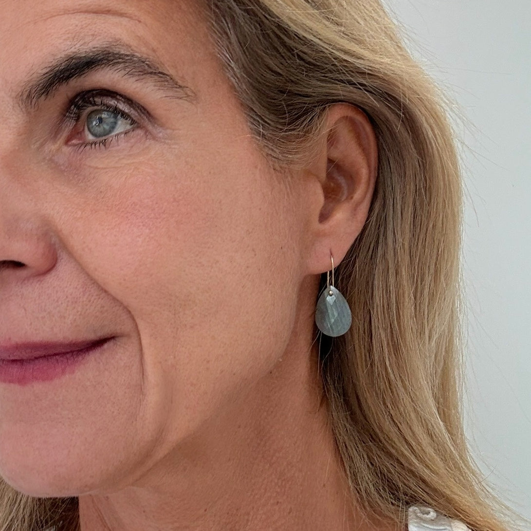 Close-up of a woman wearing a labradorite genmstone earring on a plain background