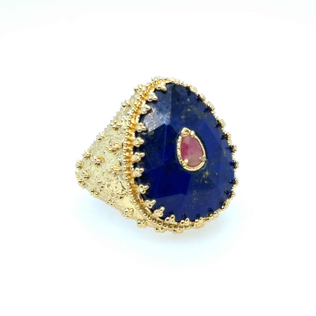A gold ring featuring a large, teardrop-shaped dark blue lapis lazuli stone with a small, teardrop-shaped pink gemstone inset in the center, set against a plain white background.