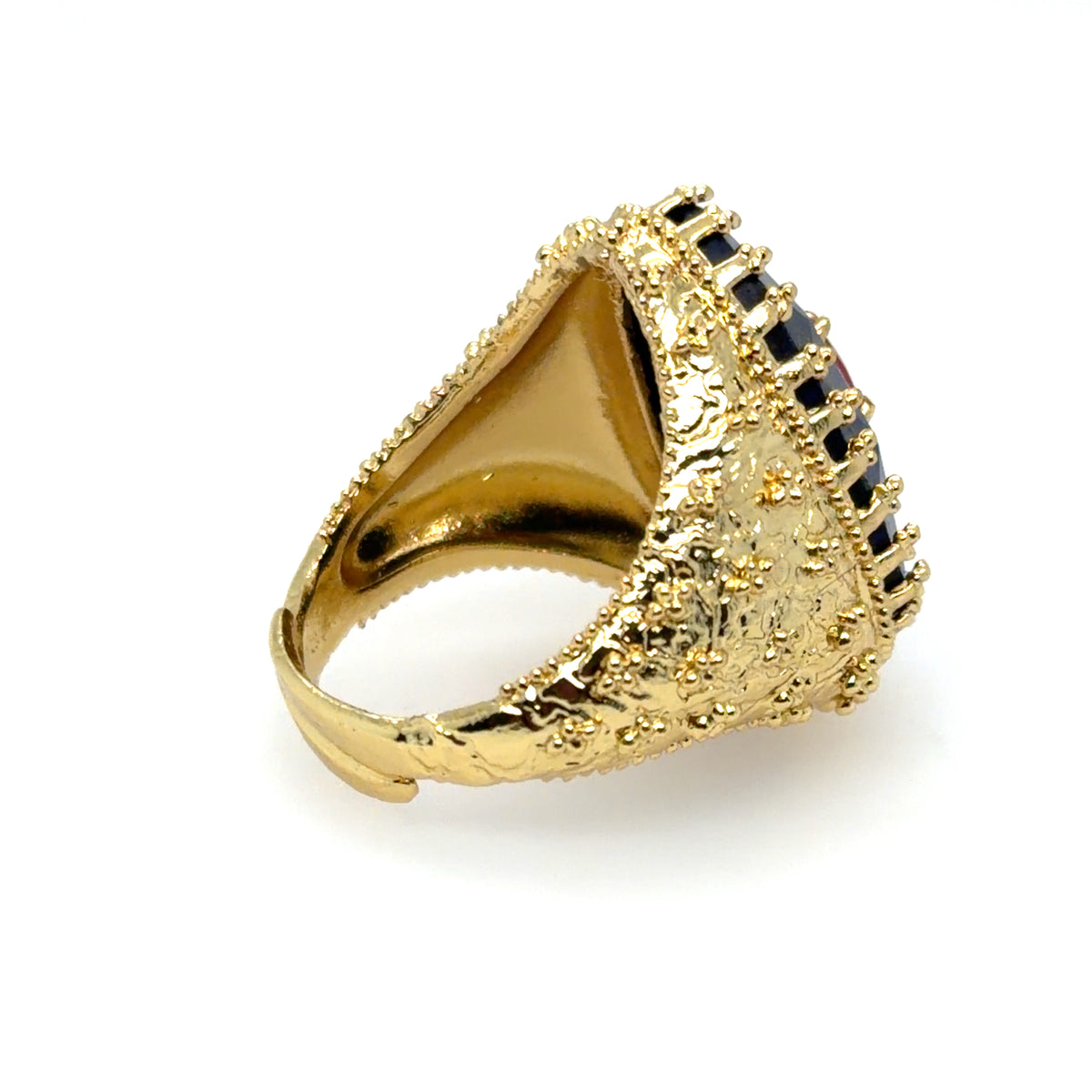 A gold signet-style ring with a textured, beaded triangular face and a border of small dark stones, shown on a plain white background.